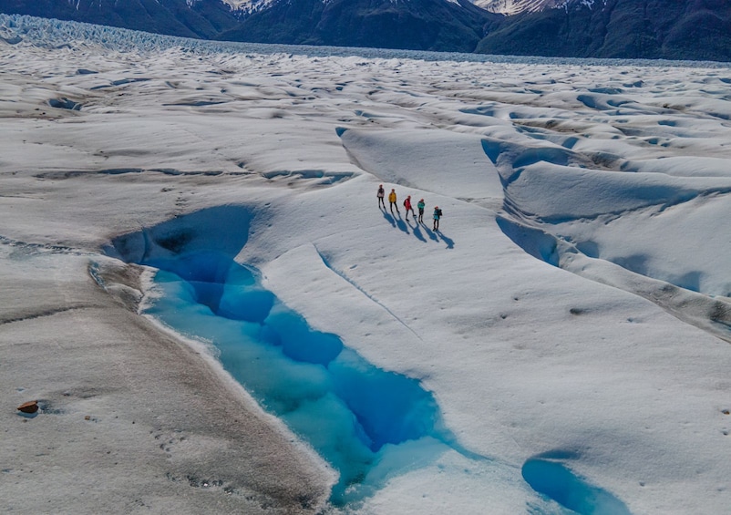 A glacier with a blue crevasse and a group of people standing on the ice. 1