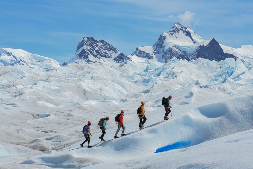 A group of hikers ascending a snow-covered mountain with glaciers and peaks in the background. 2