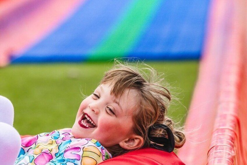 A child lying on a colorful slide with a grassy field in the background. 2