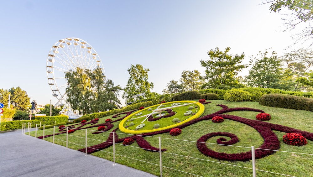 Un parco con una grande ruota panoramica, giardini curati e una statua. 5