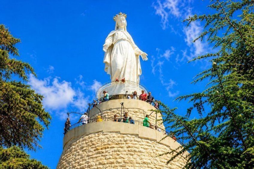 Una estatua blanca grande sobre una estructura de piedra cilíndrica, con gente alrededor. 3