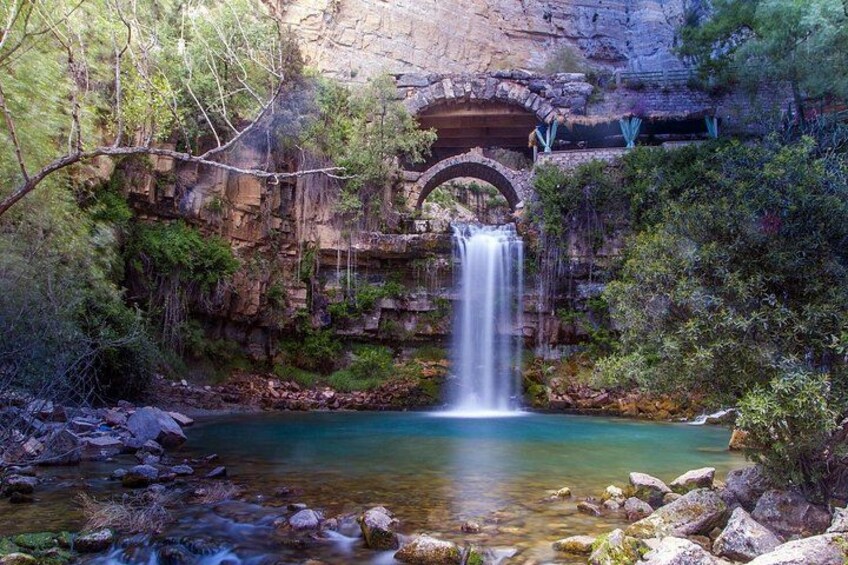 A waterfall, a clear blue pool, and a stone bridge. 1