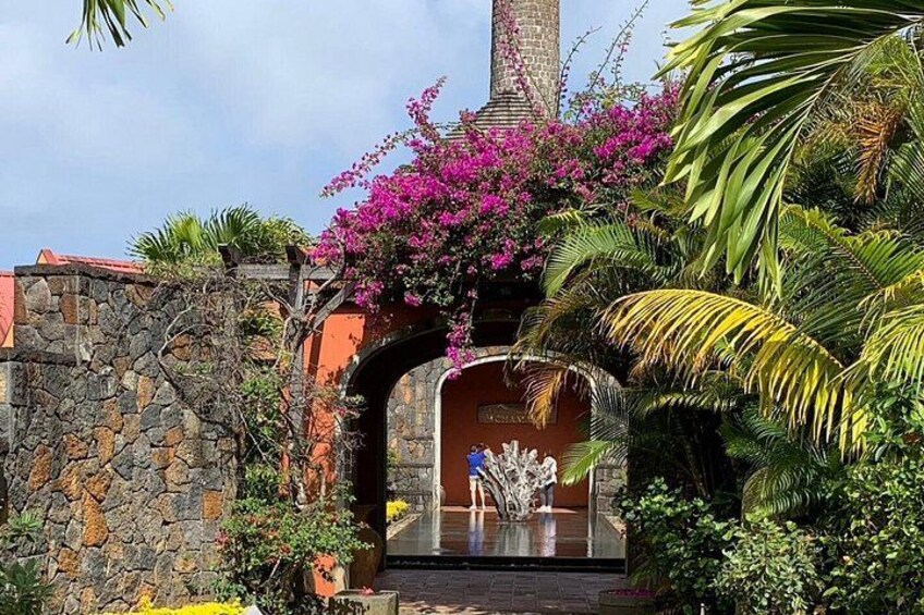 A stone archway with a statue, surrounded by lush greenery and pink flowers. 3