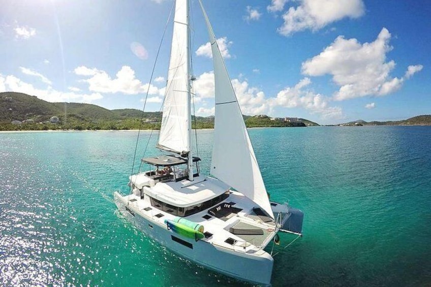 A sailboat on turquoise water with a clear sky and distant hills. 1