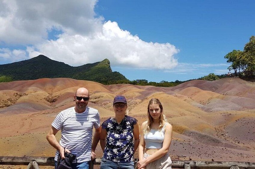 Three people standing in a landscape with reddish-brown hills and a clear sky. 2