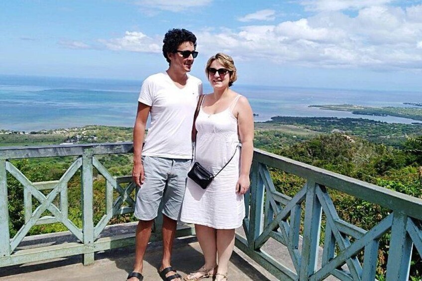 Two people standing on a bridge with a scenic view of the ocean and landscape. 1