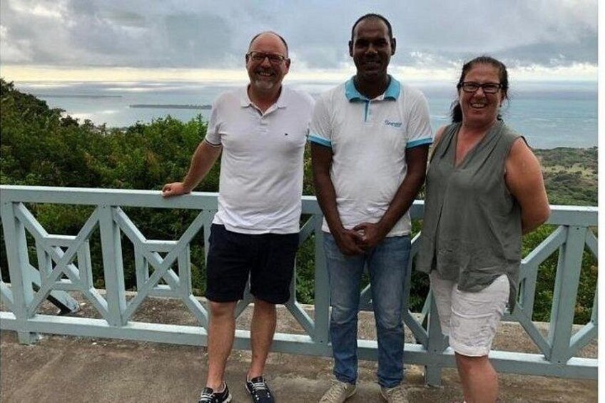 Trois personnes se tiennent sur un pont, d’où l’on peut admirer un magnifique paysage sur l’océan et les collines en arrière-plan. 2
