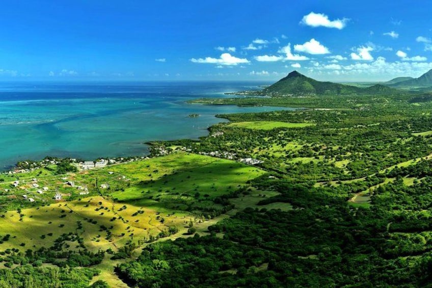 A coastal landscape with a mountain, clear blue sky, and green vegetation. 1