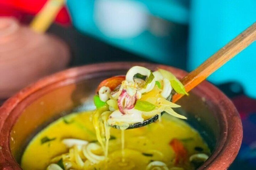 A bowl of yellow soup with noodles, garnished with green onions and red chili slices. 1