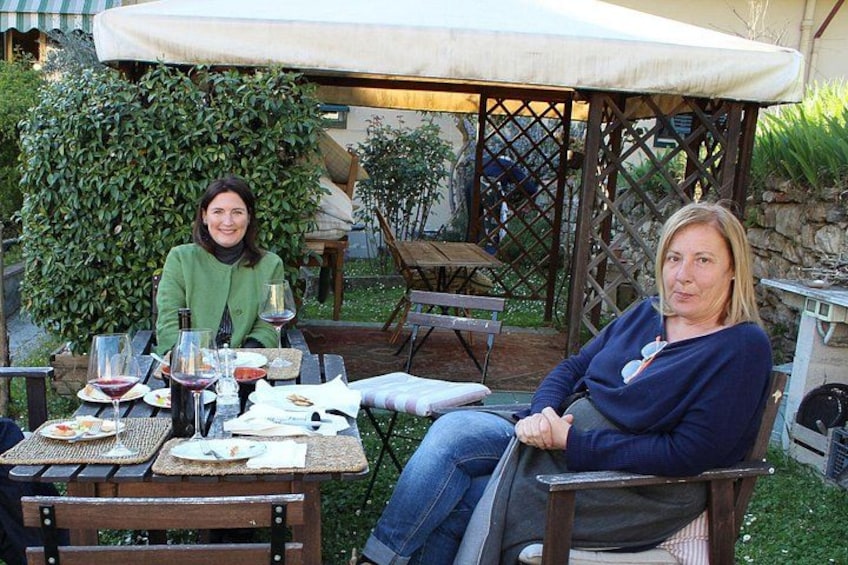 Two people seated at an outdoor table with wine glasses and plates, under a pergola. 1