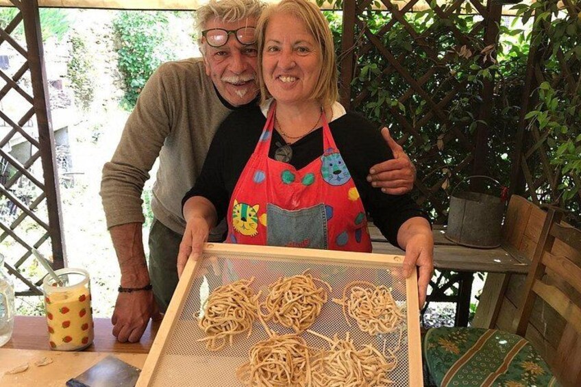 Dos personas de pie detrás de una mesa con un colador lleno de pasta. 1