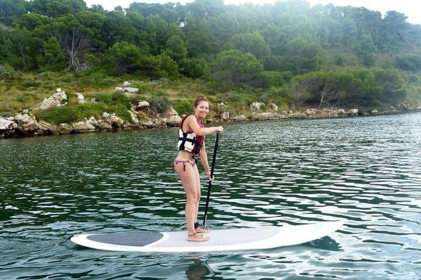 A person paddleboarding on a calm body of water with a forested shoreline in the background. 2