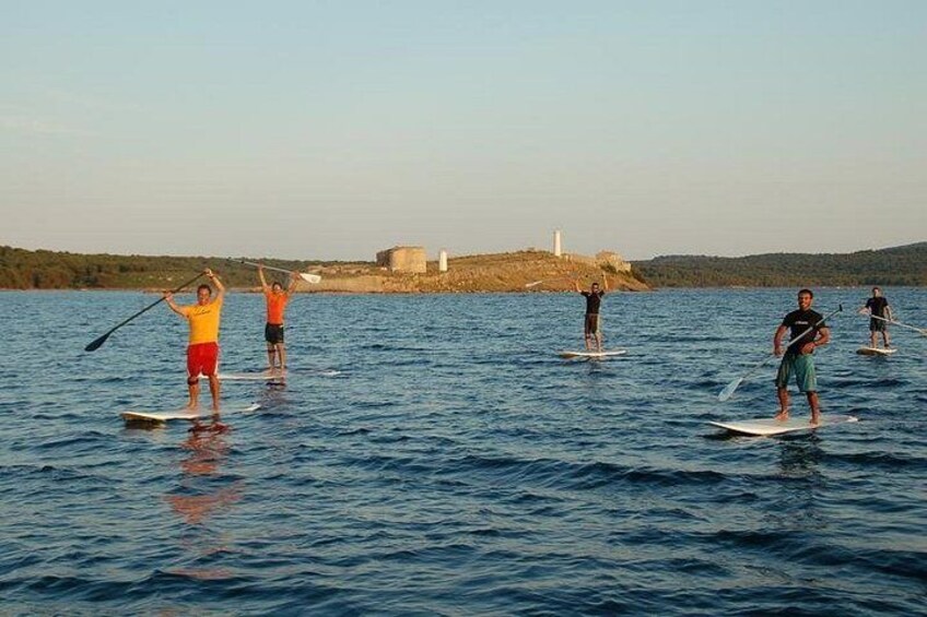 People paddleboarding on a calm body of water with a lighthouse in the background. 1