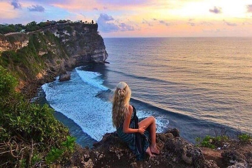 A person sitting on a cliff overlooking a coastline with waves crashing against the rocks. 5