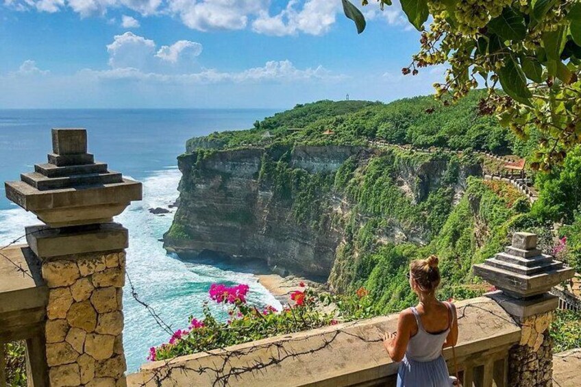 A coastal cliff with a woman standing on a stone balustrade overlooking the ocean. 3