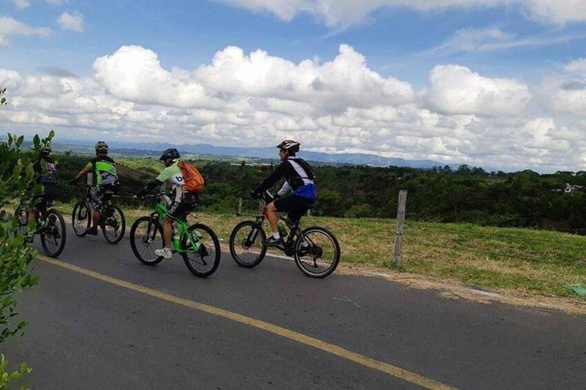 A group of cyclists on a paved road with a grassy area on one side and a hilly landscape in the background. 4