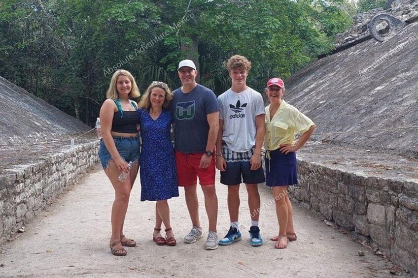 A group of people standing on a dirt path with stone walls and greenery in the background. 2
