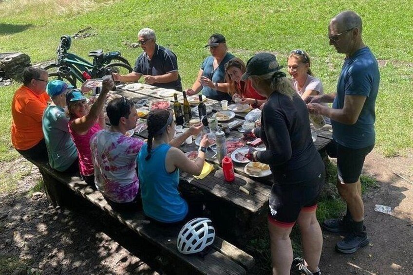 En gruppe mennesker samlet omkring et picnicbord udendørs, cykler og en cykelhjelm er synlige. 2
