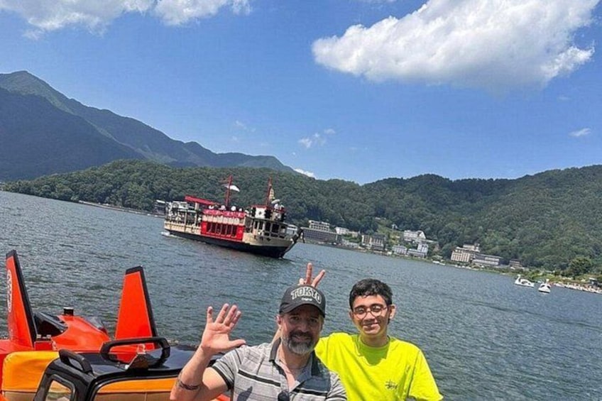 Two people on a boat with a red and white ferry in the background and mountains. 5