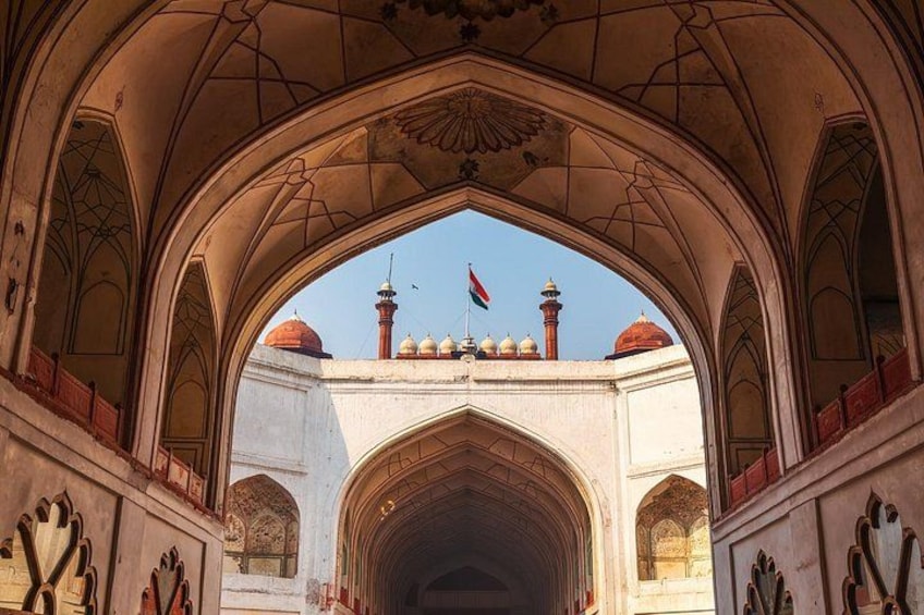 An arched corridor with intricate architectural details, leading to a domed structure with a flag. 4