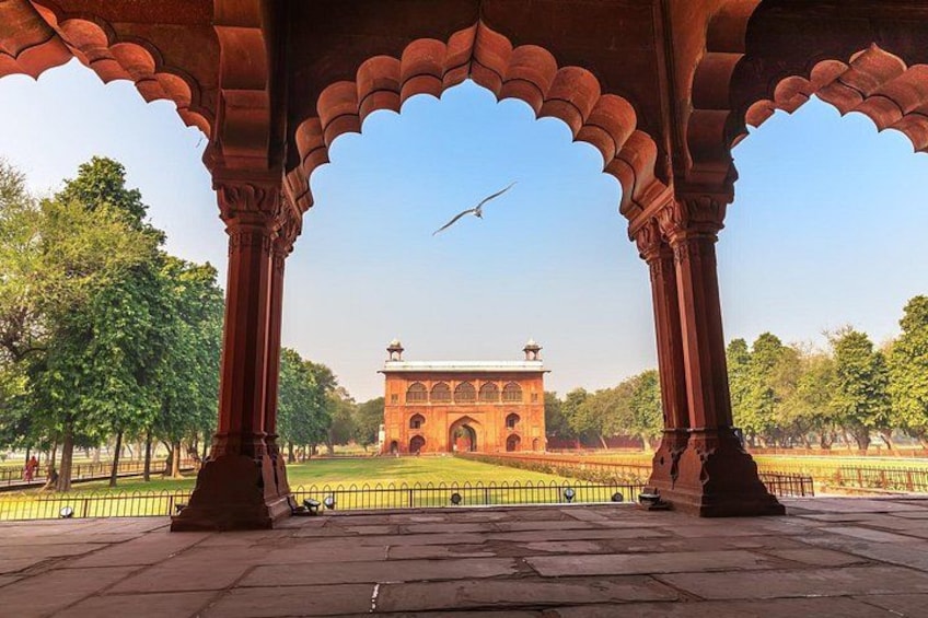 A historical building with arches and columns, a fenced area, and trees in the background. 2