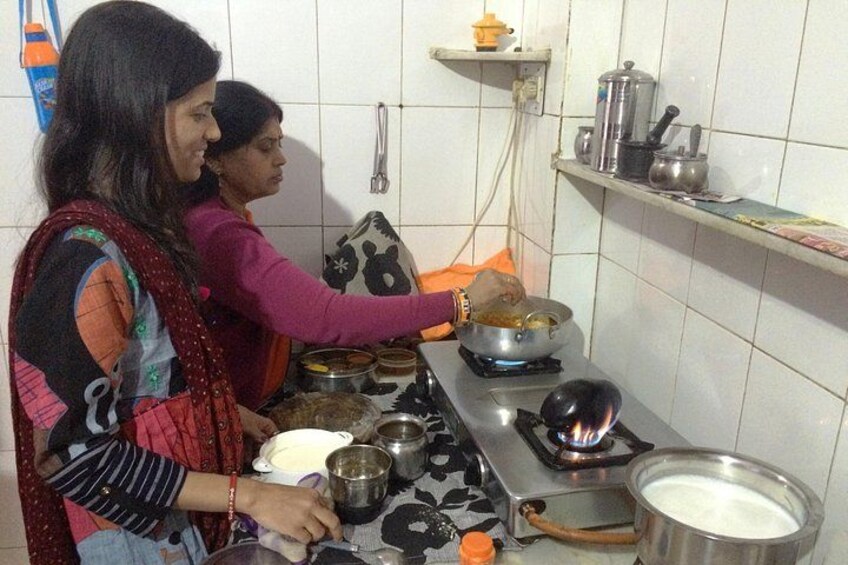 Two women cooking in a kitchen with a gas stove, pots, and a variety of cooking utensils. 4