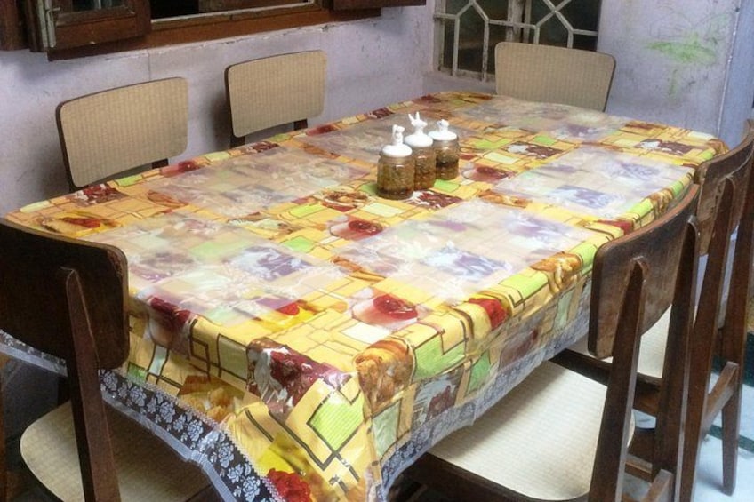 A dining table with a colorful tablecloth, four chairs, and three condiment jars. 3