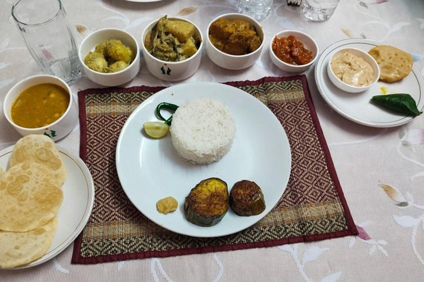A plate of white rice with two curry dishes and a flatbread, surrounded by various side dishes on a tablecloth. 2