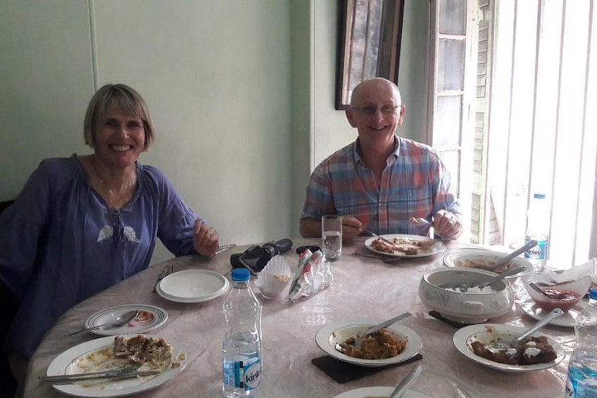 Two people sitting at a table with plates of food, a bottle of water, and a glass. 1