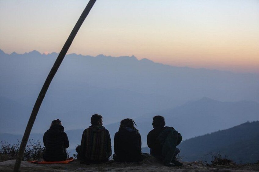 Tres personas sentadas en un saliente rocoso con vistas a una cadena montañosa. 2