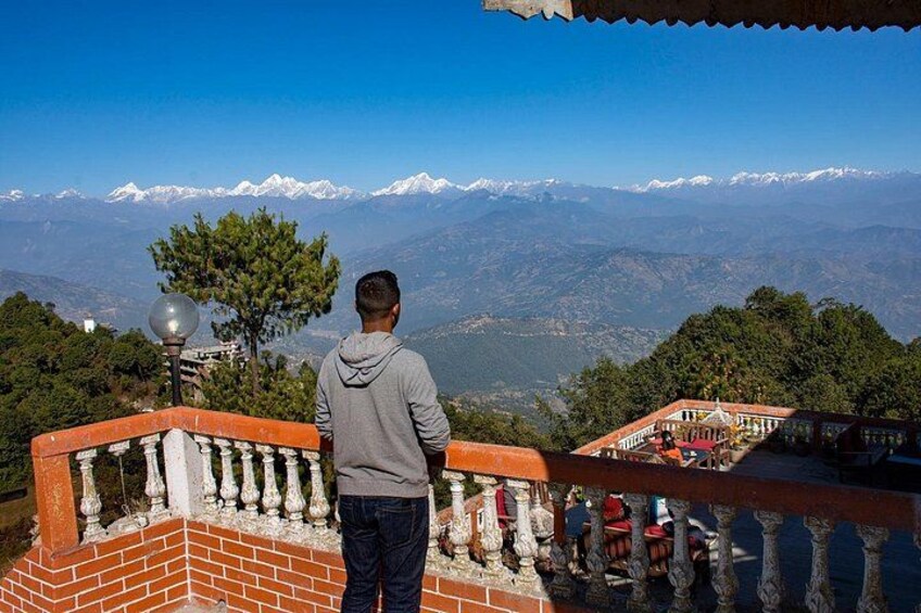 Una persona parada en un balcón que domina un paisaje montañoso con picos nevados al fondo. 5