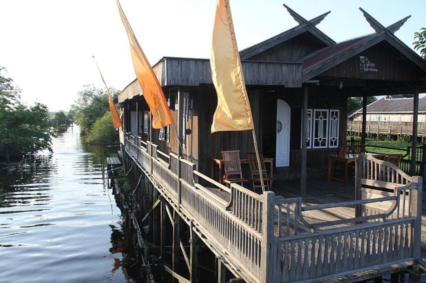A wooden structure with a deck extending over water, orange flags, and a small building with a door. 1