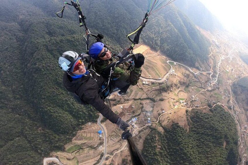 Two people skydiving over a mountainous landscape with visible roads and buildings below. 4