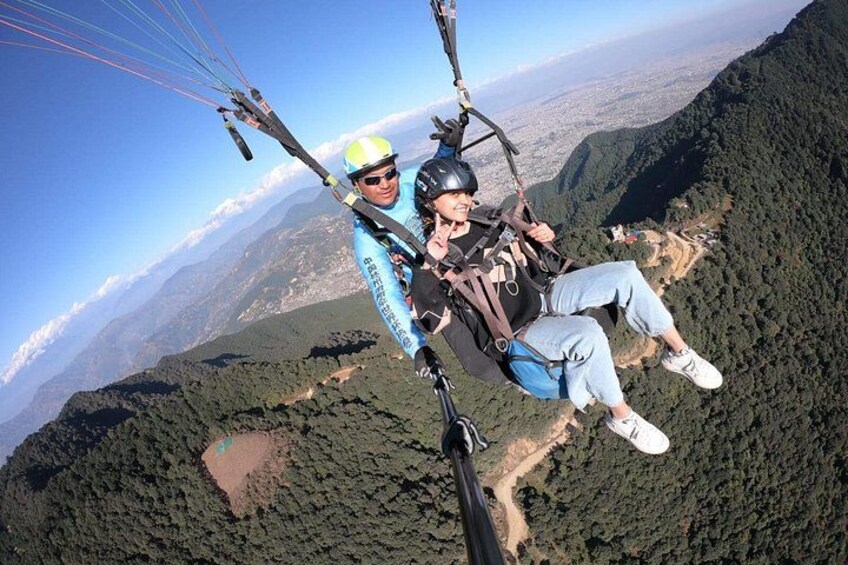 A person paragliding over a mountainous landscape with dense forests and a clear sky. 1