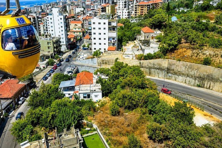 A yellow cable car, a road, and a coastal cityscape with buildings and greenery. 2