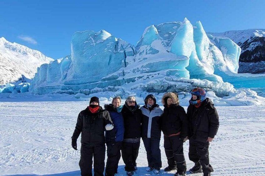 A group of people standing on snow with icebergs in the background. 2