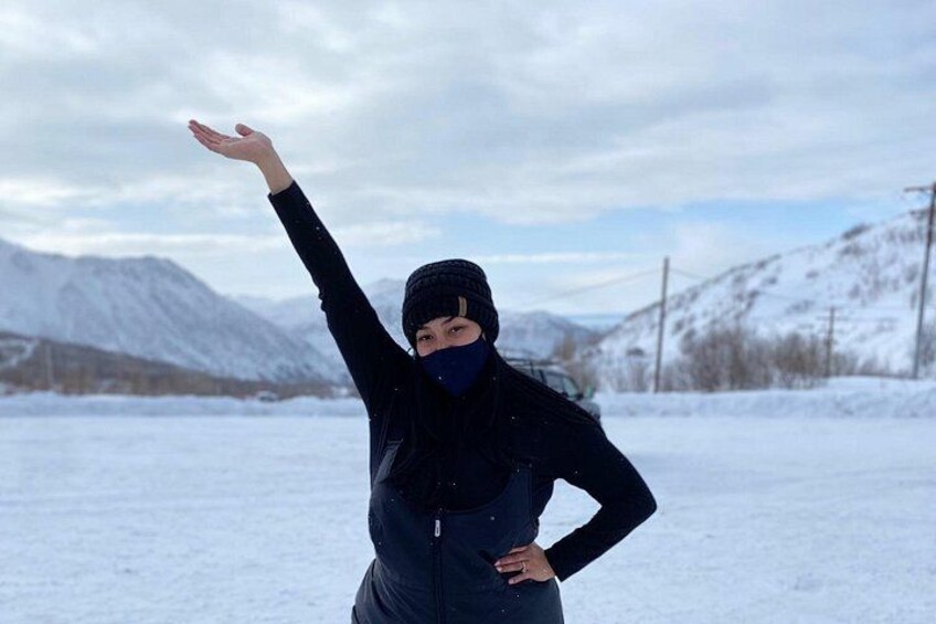 A person in a black jacket and beanie standing in a snowy landscape with mountains in the background. 5