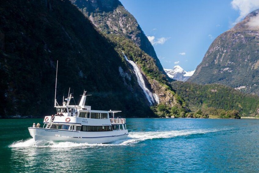 A boat on a calm lake surrounded by steep mountains and a waterfall. 3