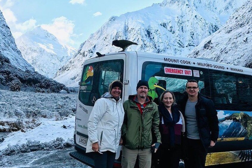 A group of people standing in front of a bus with a snowy mountainous landscape in the background. 1