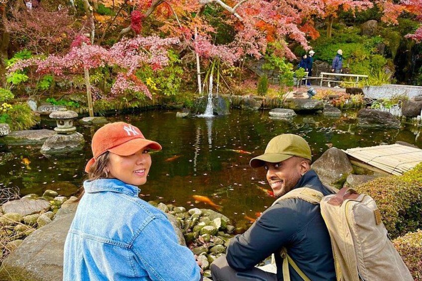 Ein Paar sitzt an einem Teich mit Koi-Karpfen, umgeben von Herbstlaub und einem Steinlaternen. 3