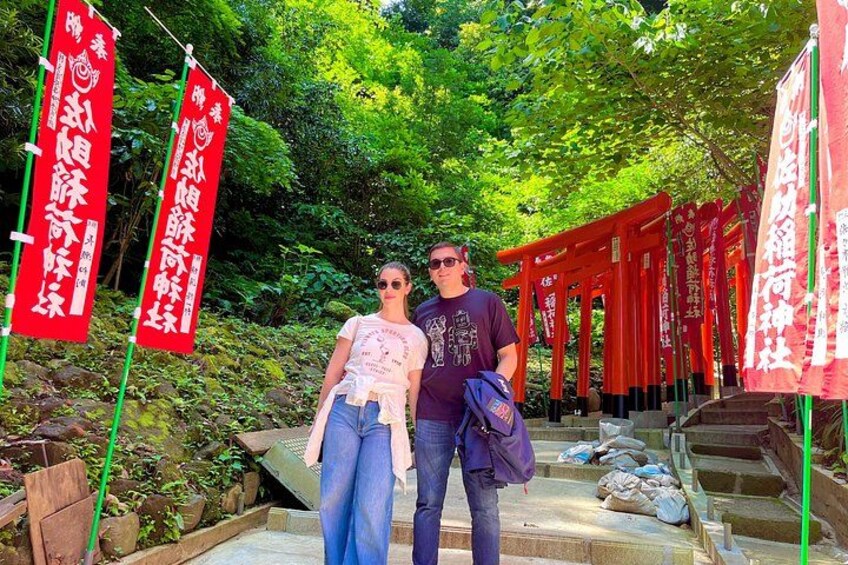 Zwei Personen stehen vor roten Torii-Toren mit japanischem Text, umgeben von viel Grün. 4