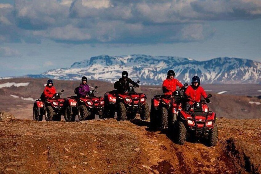 Un gruppo di persone su veicoli ATV su un sentiero sterrato, con montagne innevate sullo sfondo. 5