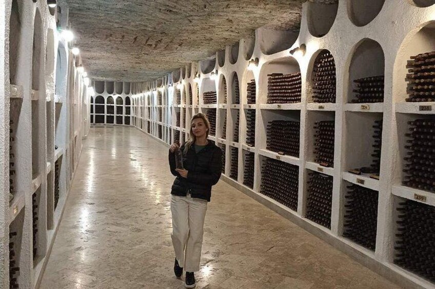 Une personne se promène dans une cave à vin, où de nombreuses bouteilles de vin sont alignées sur des étagères. 3
