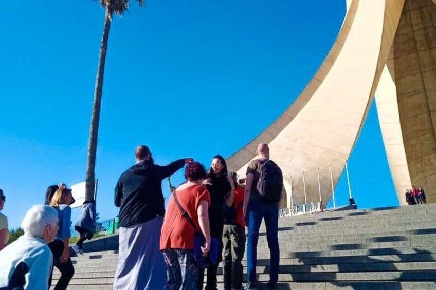 A group of people standing on steps with a large, curved architectural structure in the background. 3
