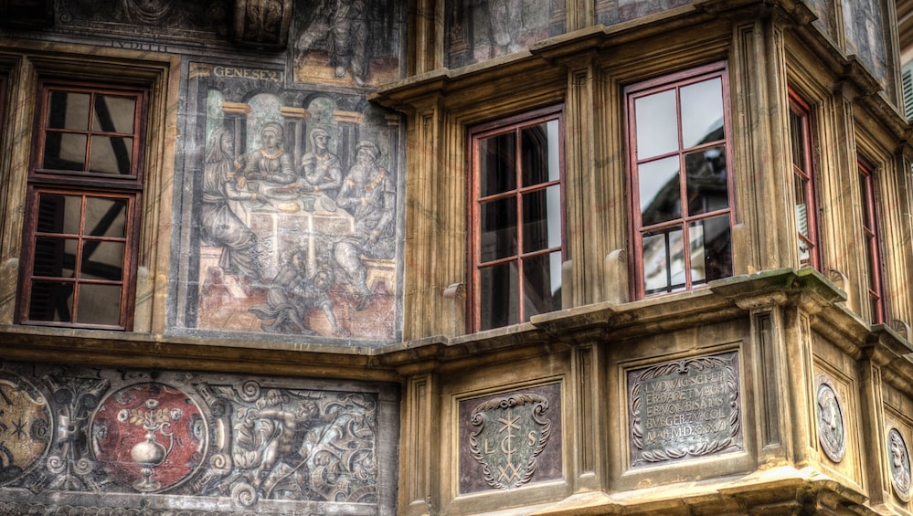 A building facade with classical architectural elements, including a detailed fresco and ornate window frames. 3