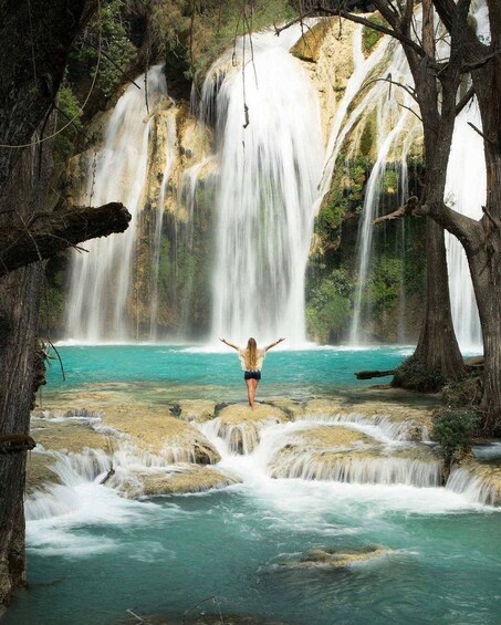 A waterfall with a person standing on rocks in the middle. 1