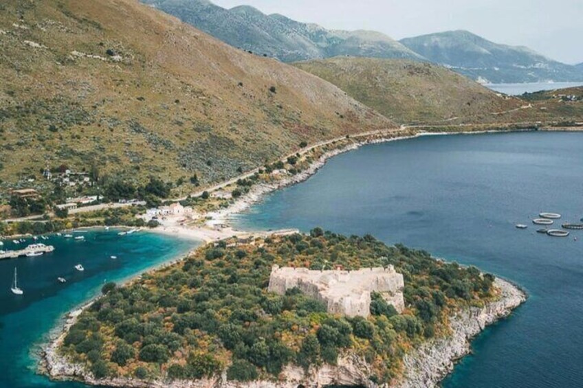 Eine Küstenlandschaft mit einer kleinen Insel, auf der sich eine Burg befindet, umgeben von klarem, blauem Wasser und Hügeln. 3