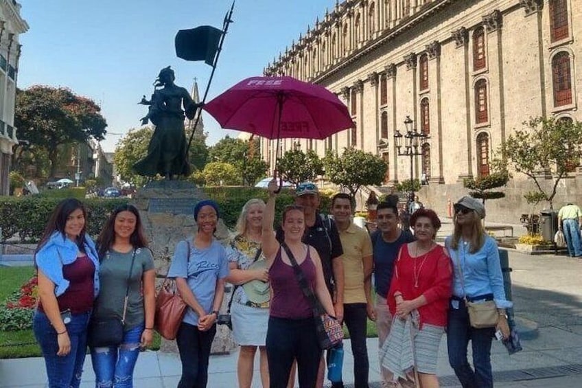 Un grupo de personas posando frente a una estatua, con un edificio al fondo. 1