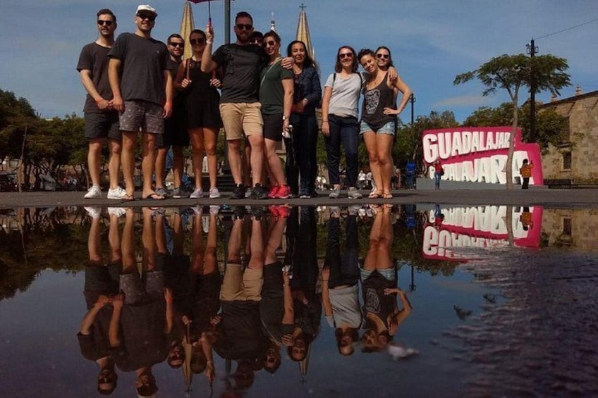 Un grupo de personas frente a una superficie acuática reflectante, con un cartel que dice 'GUADALAJAR'. 2