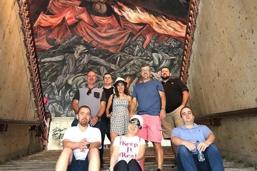 Un grupo de personas de pie en una escalera con un mural grande al fondo. 5